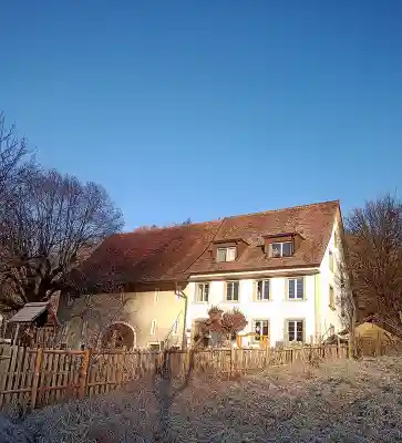 Das grosse weisse Bauernhaus des Seehofs mit Ziegeldach an einem frostigen Morgen unter blauem Himmel, davor ein Holzzaun.
